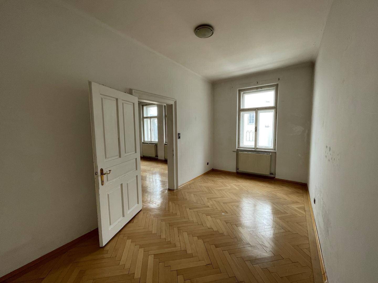 Helles, unmöbliertes Zimmer mit Fischgrätparkett und hohen Decken im Altbau.