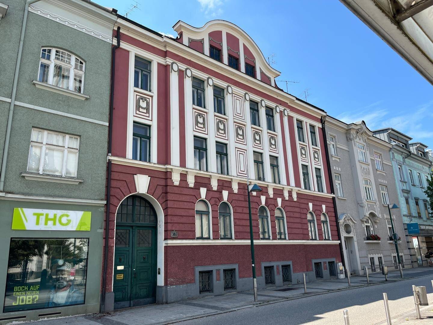 Historisches Gebäude mit roter und weißer Fassade an einer städtischen Straße unter blauem Himmel.