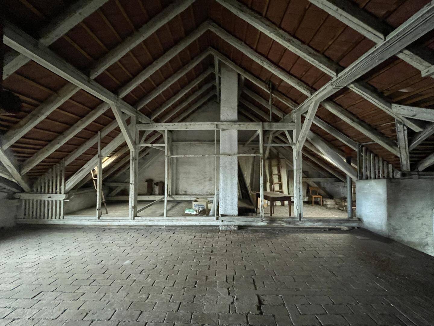 Großer Dachbodenbereich mit freiliegenden Holzbalken und Ziegelboden, bietet viel Potenzial.