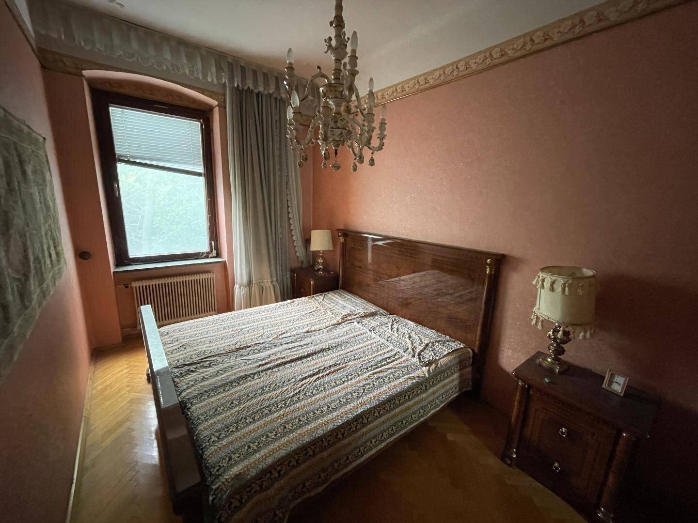 Schlafzimmer mit klassischem Doppelbett, rosa Wänden, Parkettboden und einem opulenten Kronleuchter.