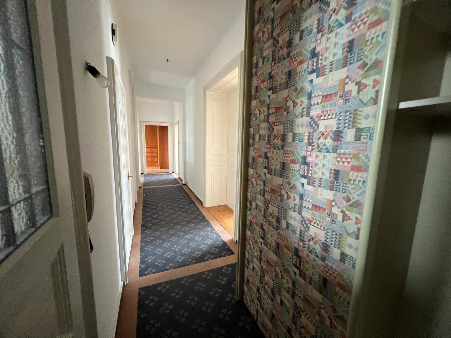 Langer Flur mit Teppichboden und gemusterter Tapete, der zu weiteren Räumen im Haus führt.