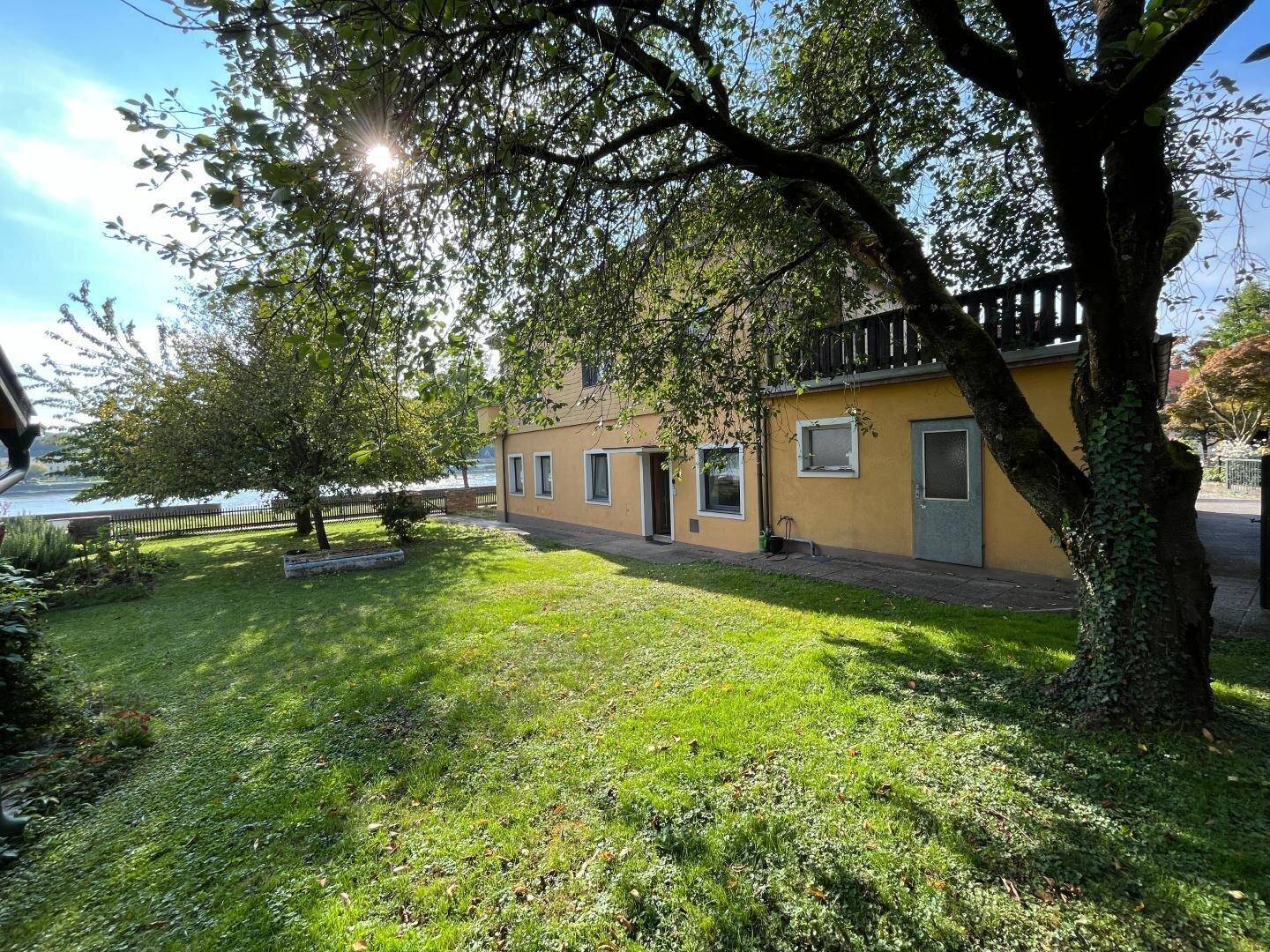 Weitläufiger Gartenbereich des Hauses mit altem Baumbestand und Blick auf das Wasser.