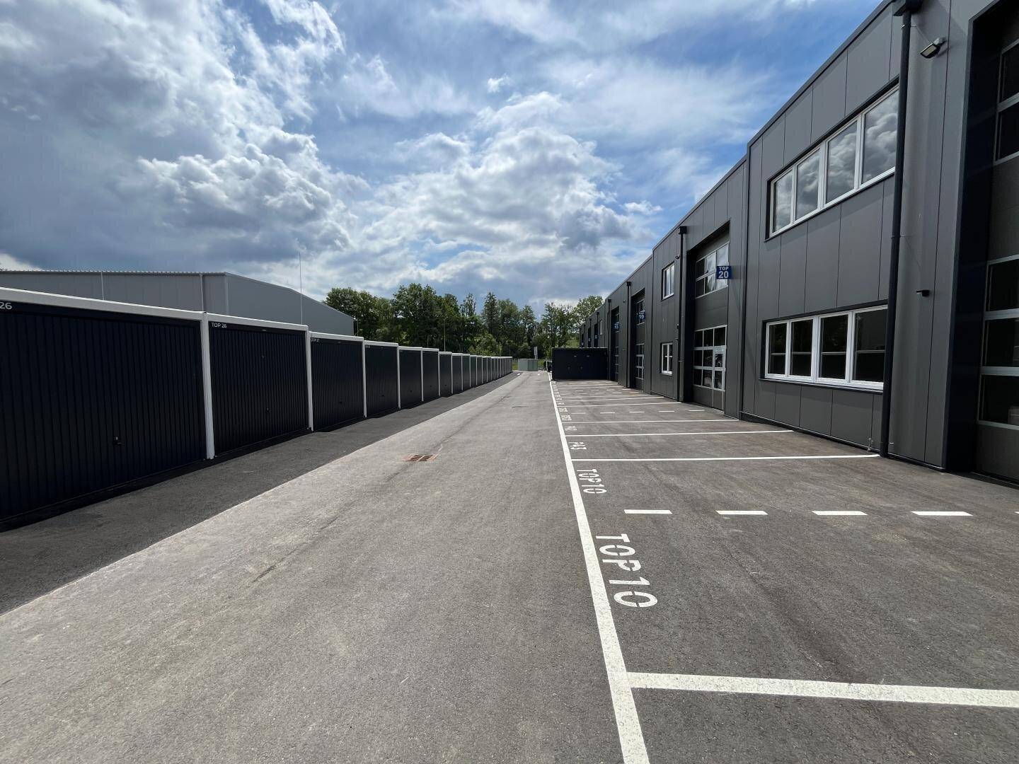Außenansicht eines modernen Gewerbegebäudes mit Parkplätzen und einer Reihe von Garagenboxen.