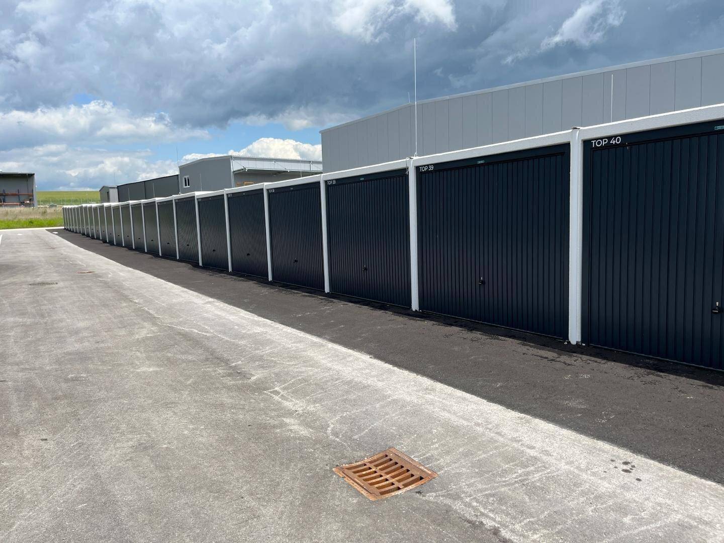 Lange Reihe von modernen Garagenboxen mit dunklen Toren und weißem Rahmen unter bewölktem Himmel.