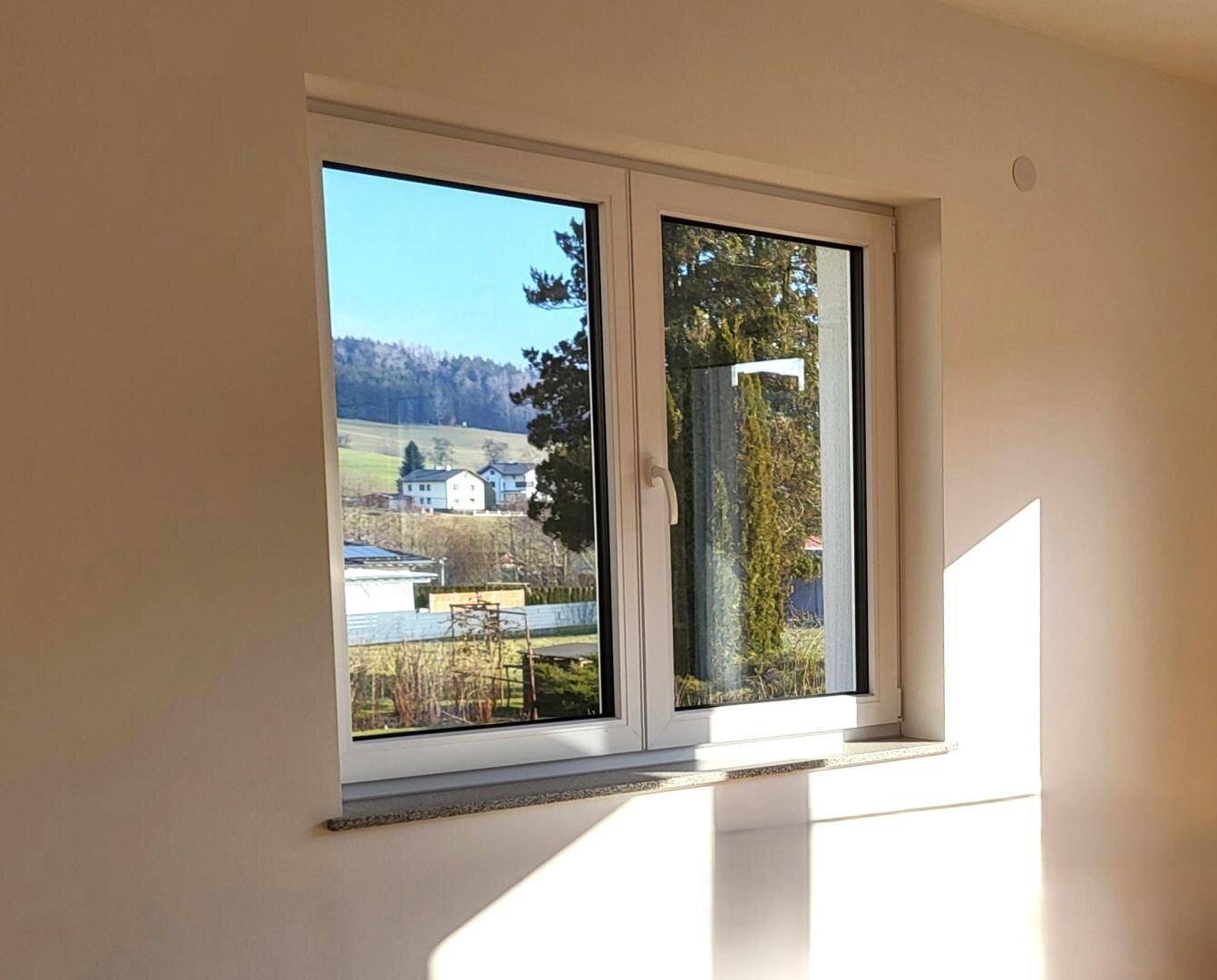 Großes Fenster in einem hellen Raum mit Blick auf die grüne Landschaft.