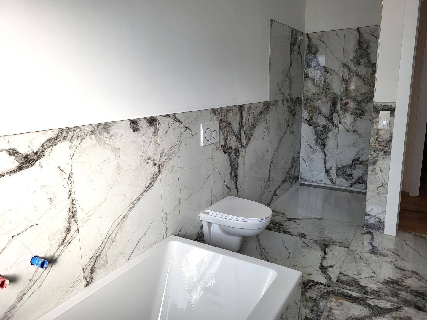 Modernes Badezimmer mit eleganten Marmorfliesen, Badewanne und wandhängendem WC.