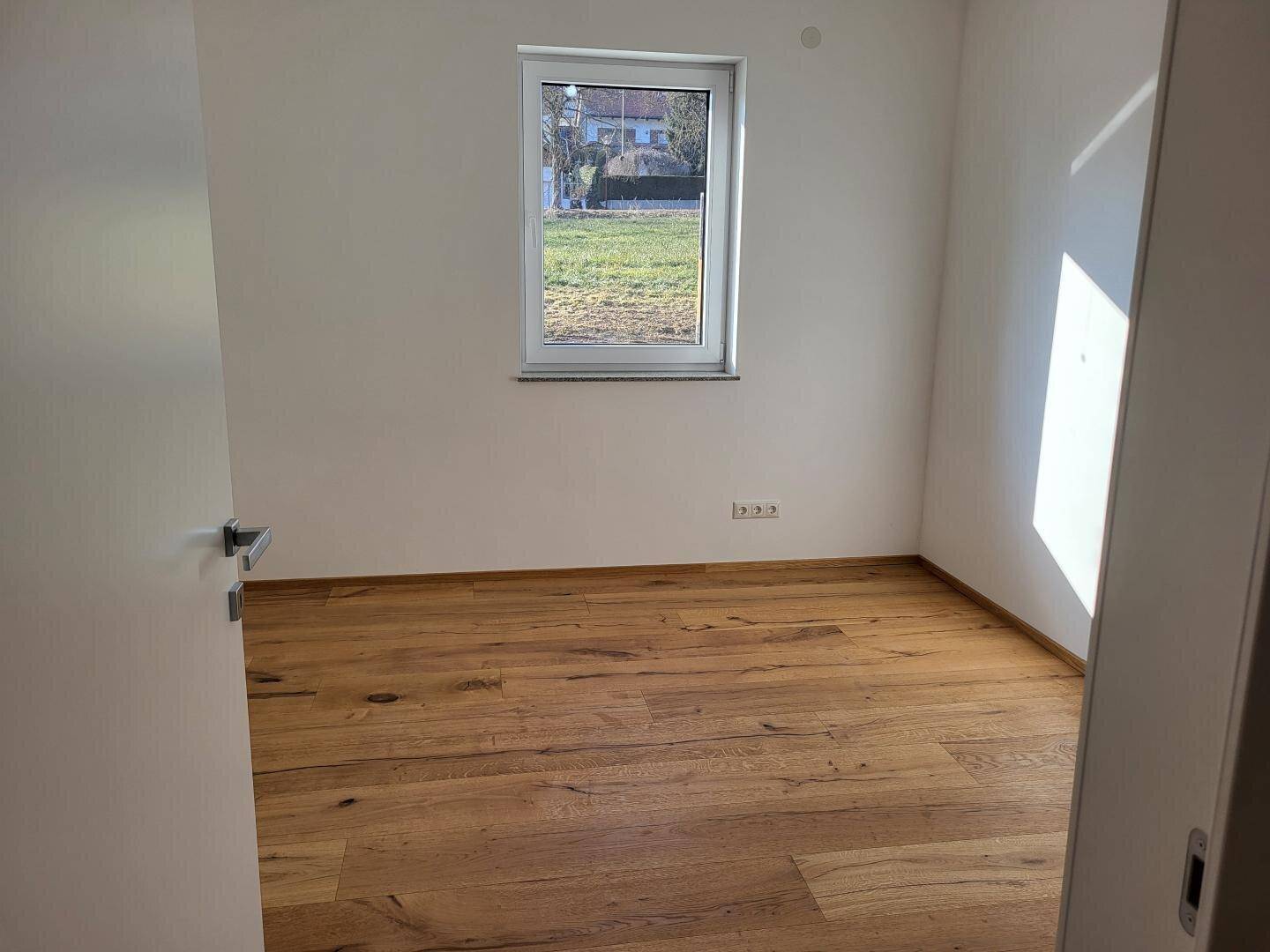 Schlafzimmer mit hellem Holzboden und einem Fenster mit Blick ins Grüne.