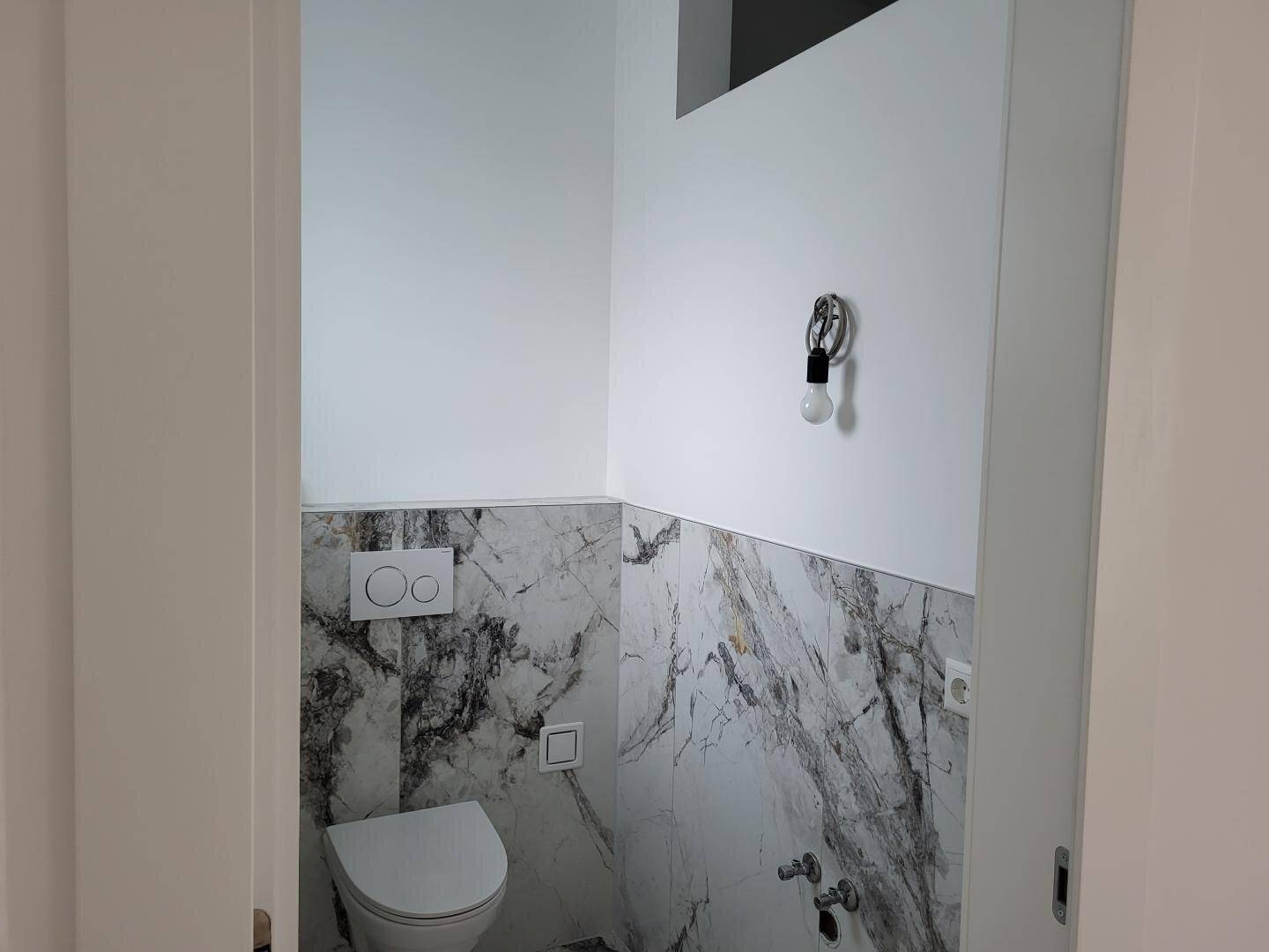 Separates Gäste-WC mit Marmorfliesen und wandhängender Toilette.