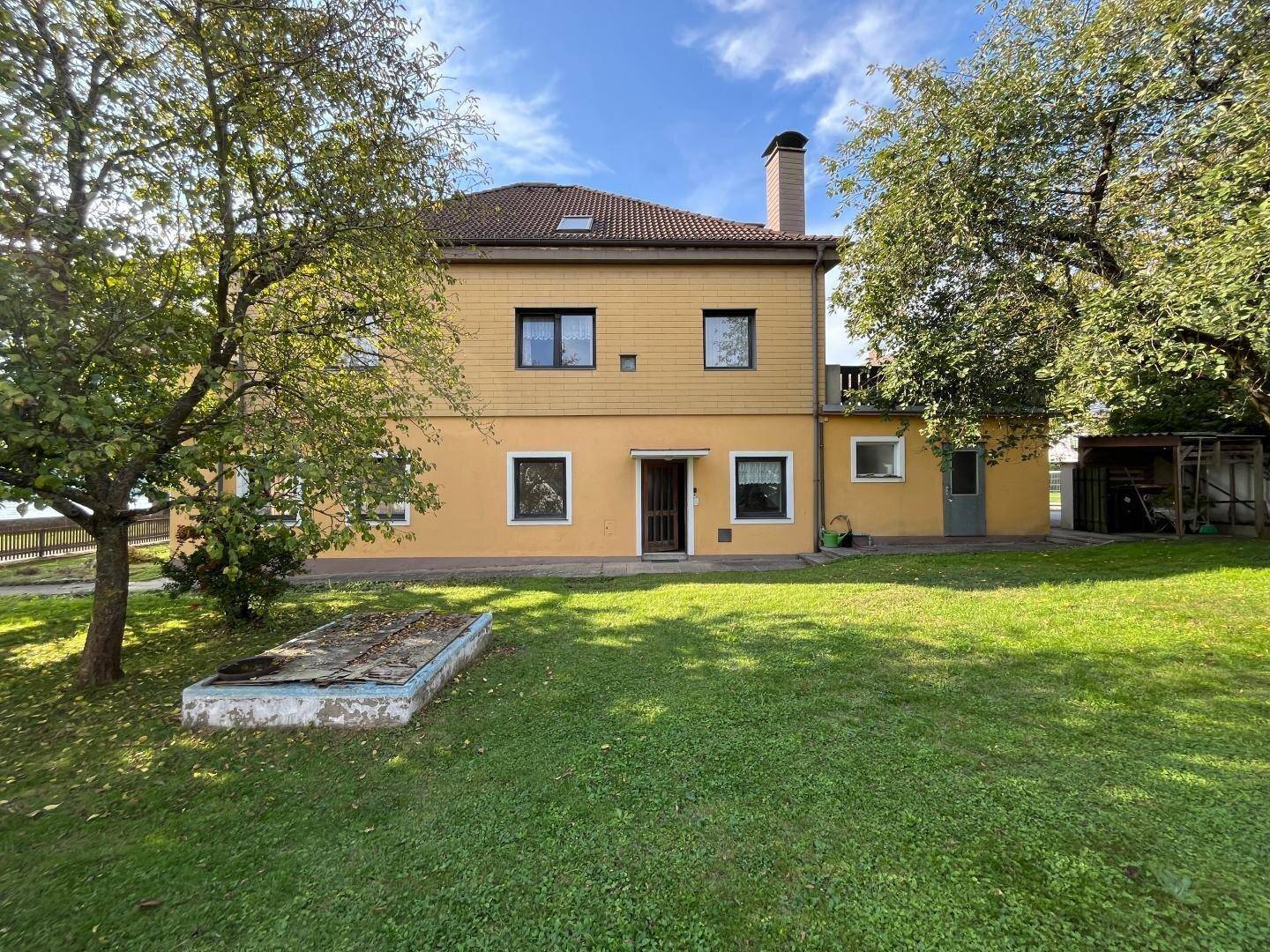Hinteransicht des Hauses mit großem Rasen, Bäumen und einem alten Wasserbecken im Garten.