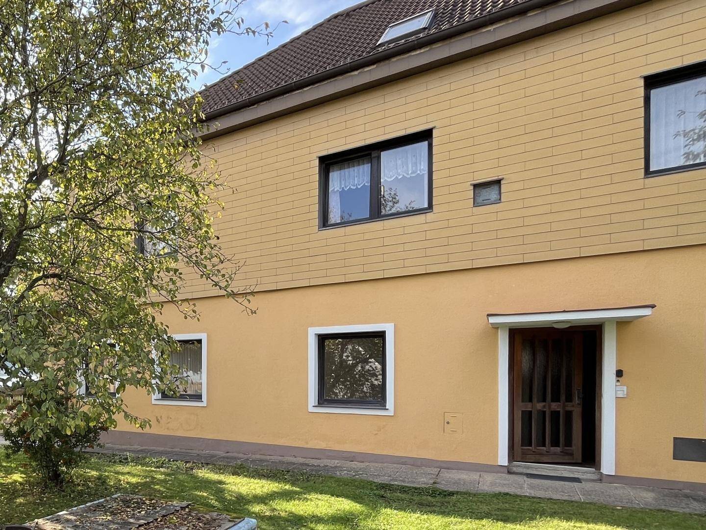 Detailansicht des Hauseingangs mit gelber Fassade, dunklen Fenstern und kleiner Überdachung.