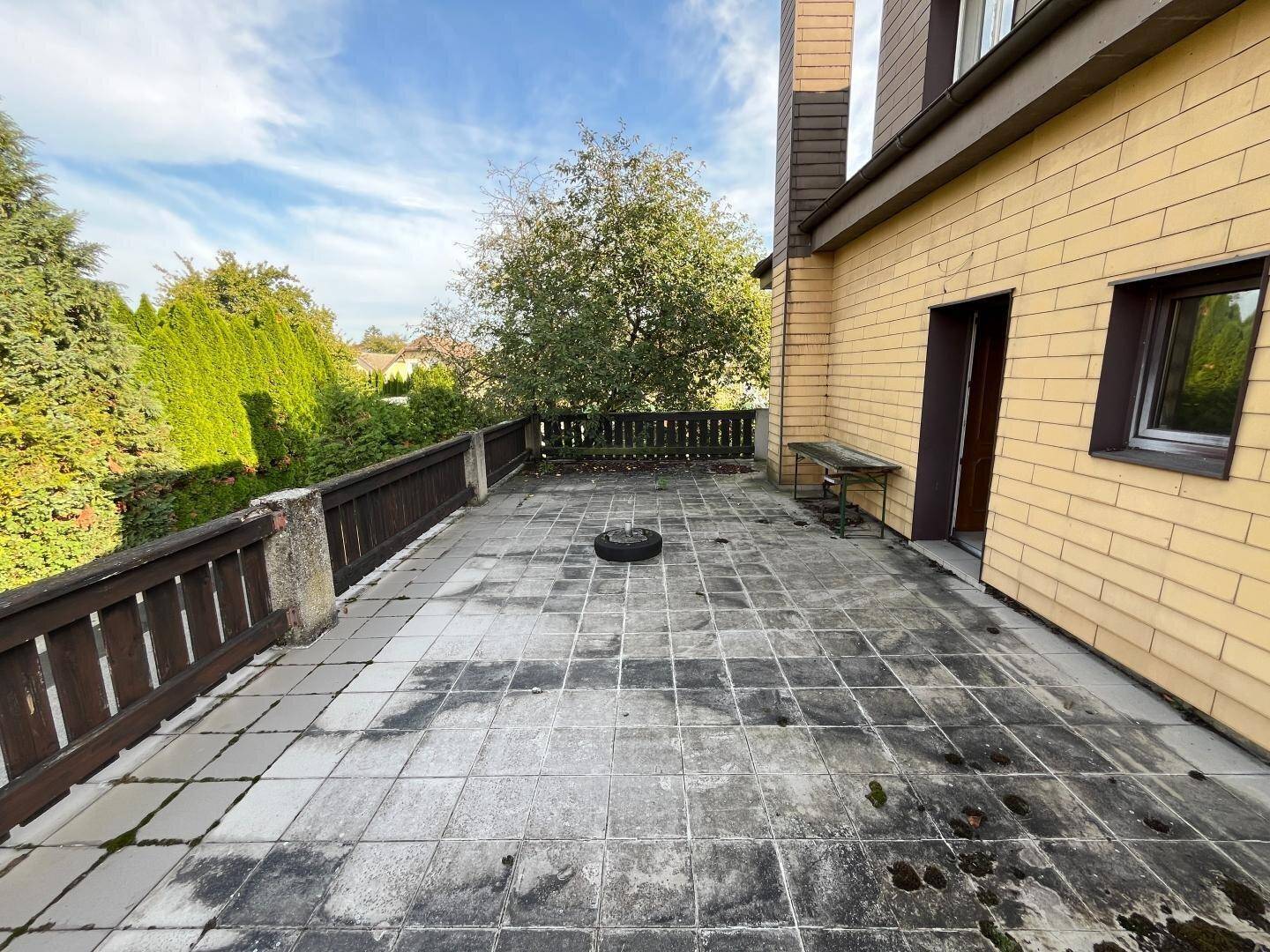 Große geflieste Terrasse mit Holzgeländer, die eine Renovierung benötigt.
