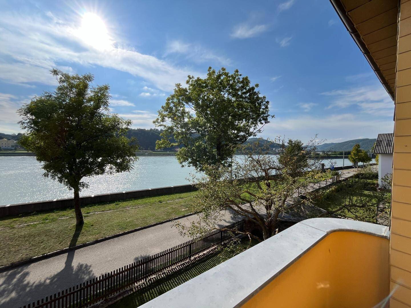 Sonnige Aussicht vom Balkon auf den Fluss, umgeben von Bäumen und blauem Himmel.