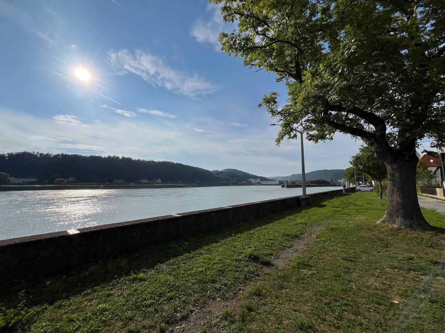 Weitläufiger Blick auf den sonnigen Fluss mit bewaldeten Hügeln im Hintergrund.