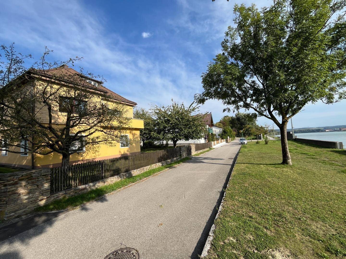Gelbes Haus an einer ruhigen Straße mit Blick auf den Fluss und grüne Ufer.