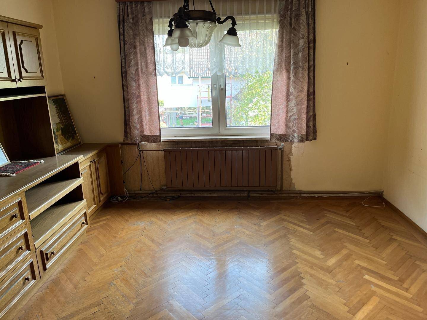 Zimmer mit Fischgrätparkett, Fenster und einem eingebauten Holzschrank.