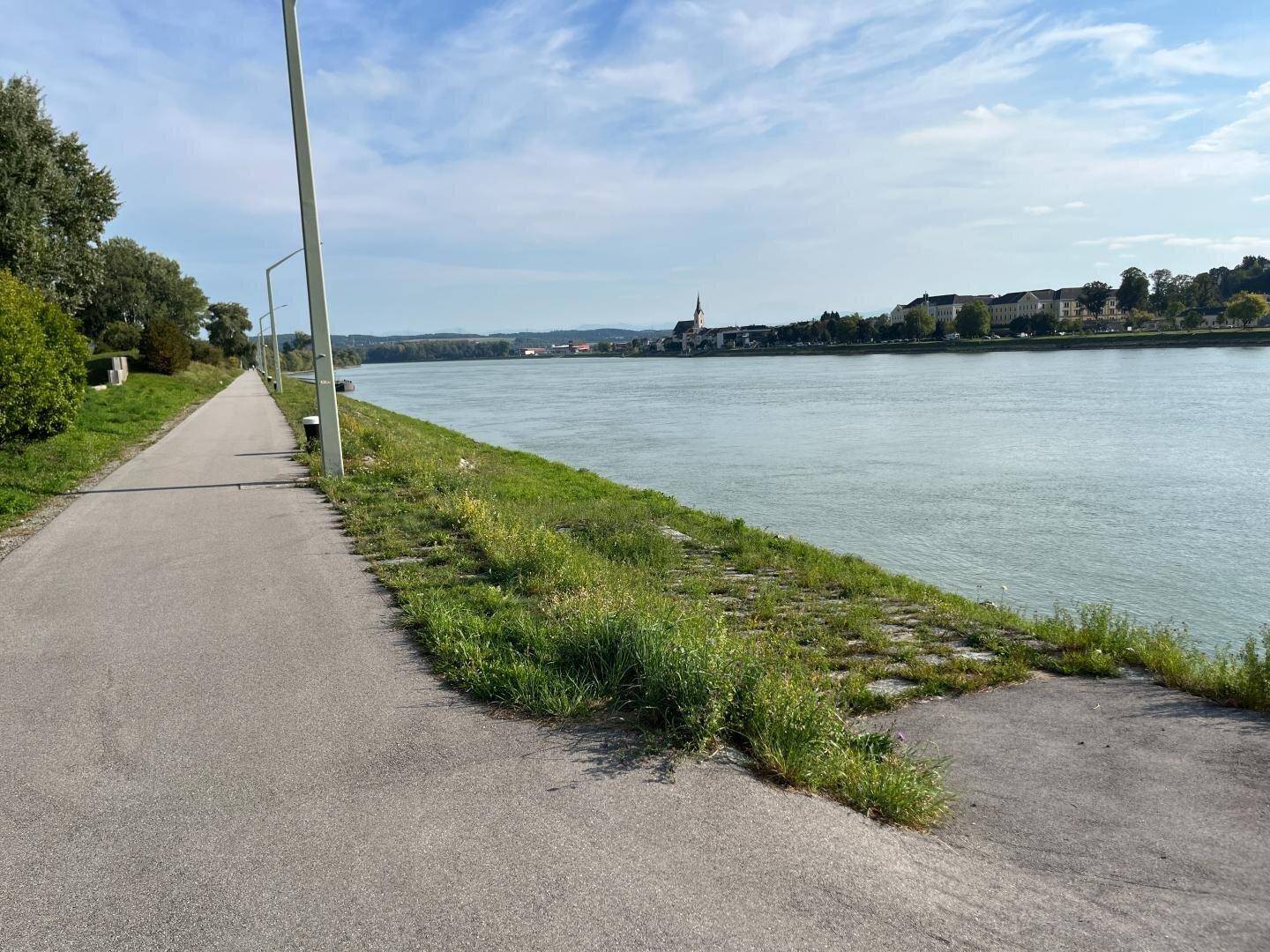 Uferweg entlang des Flusses mit Blick auf eine Kirche in der Ferne.