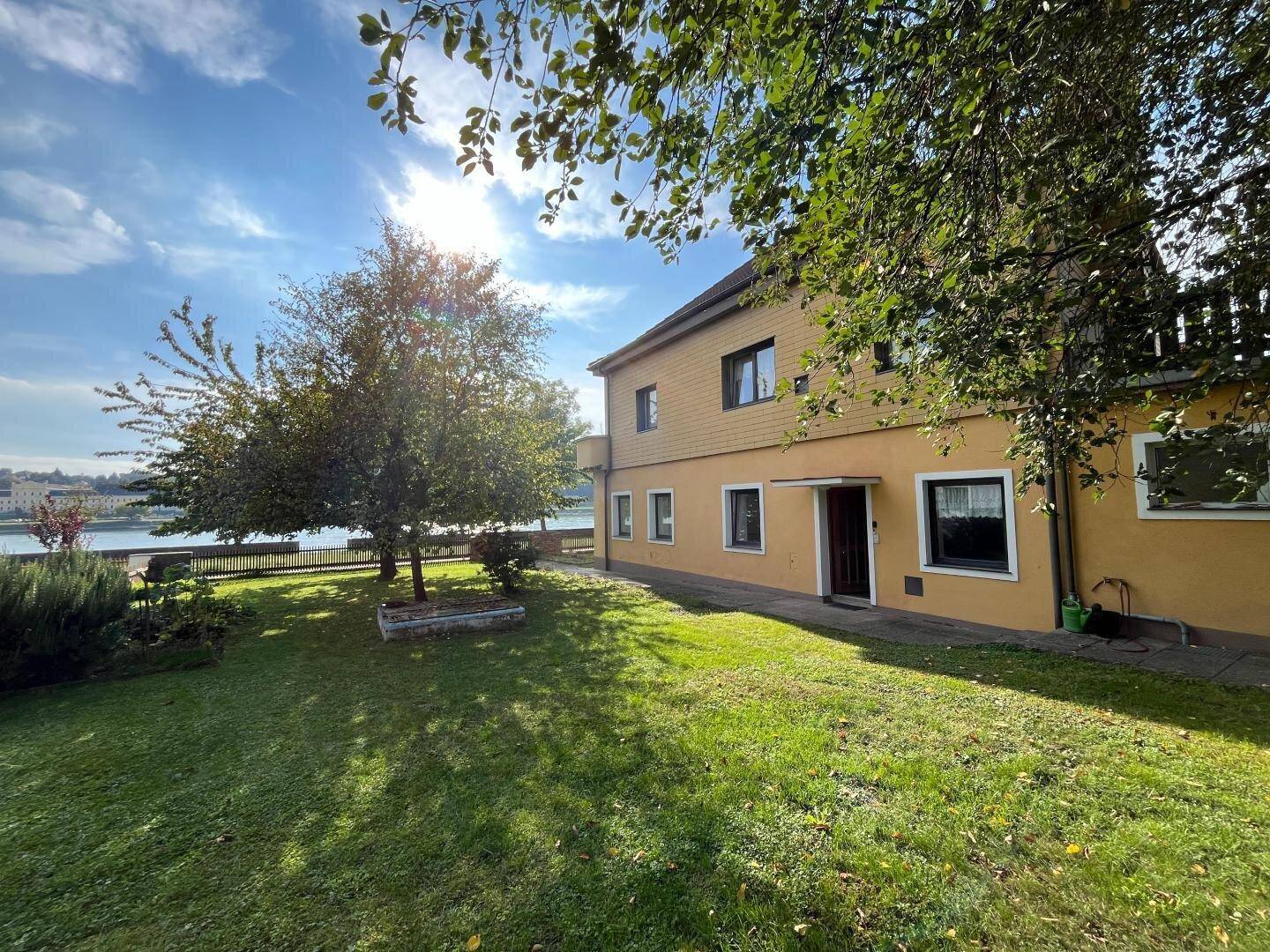 Sonnige Gartenansicht des Hauses mit Blick auf den Fluss und üppiges Grün.