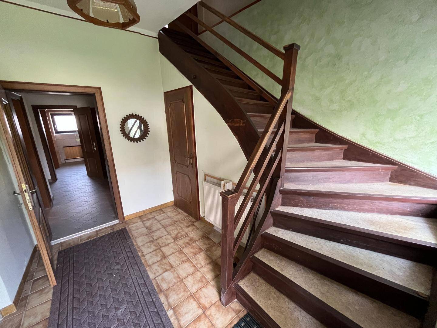 Eingangsbereich mit rustikaler Holztreppe, gefliestem Boden und grün gestrichenen Wänden.