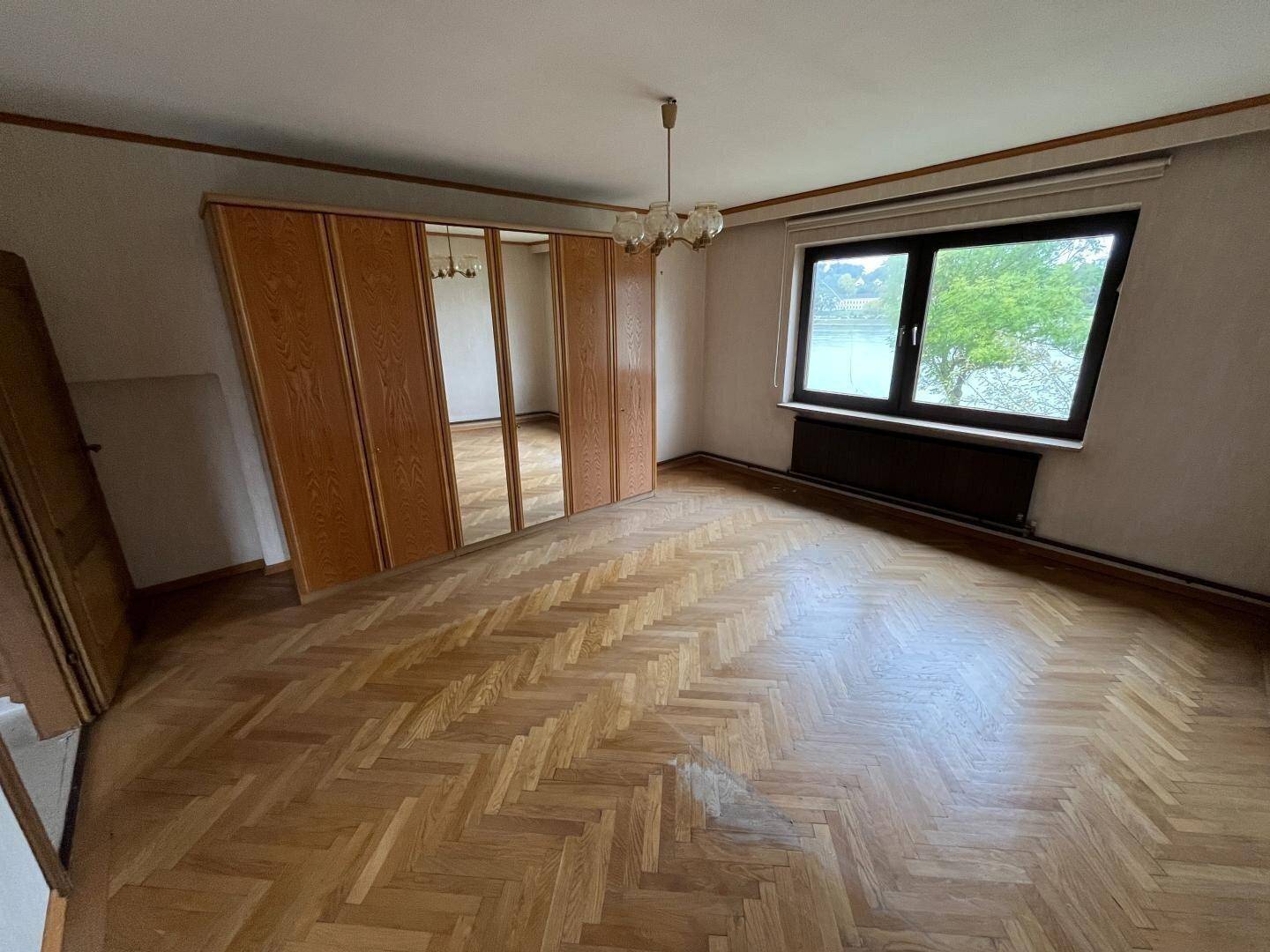 Schlafzimmer mit Fischgrätparkett, großem Spiegelschrank und Blick ins Grüne.