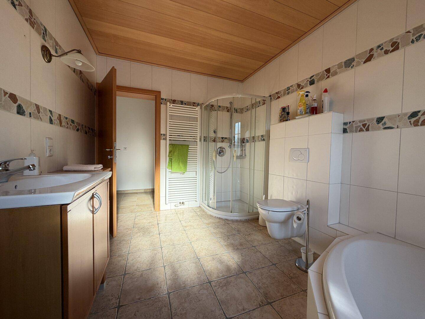 Badezimmer mit Duschkabine, WC, Waschbecken, Holzdecke und beheiztem Handtuchhalter.