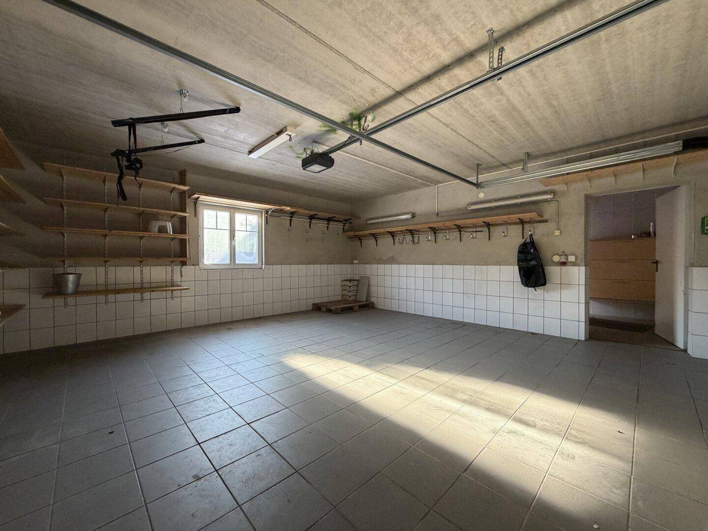 Geräumige Garage mit Fliesenboden, Regalen und einem Fenster für Tageslicht.