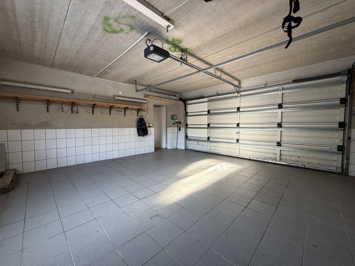 Große Garage mit offenem Garagentor, Fliesenboden und viel Platz.