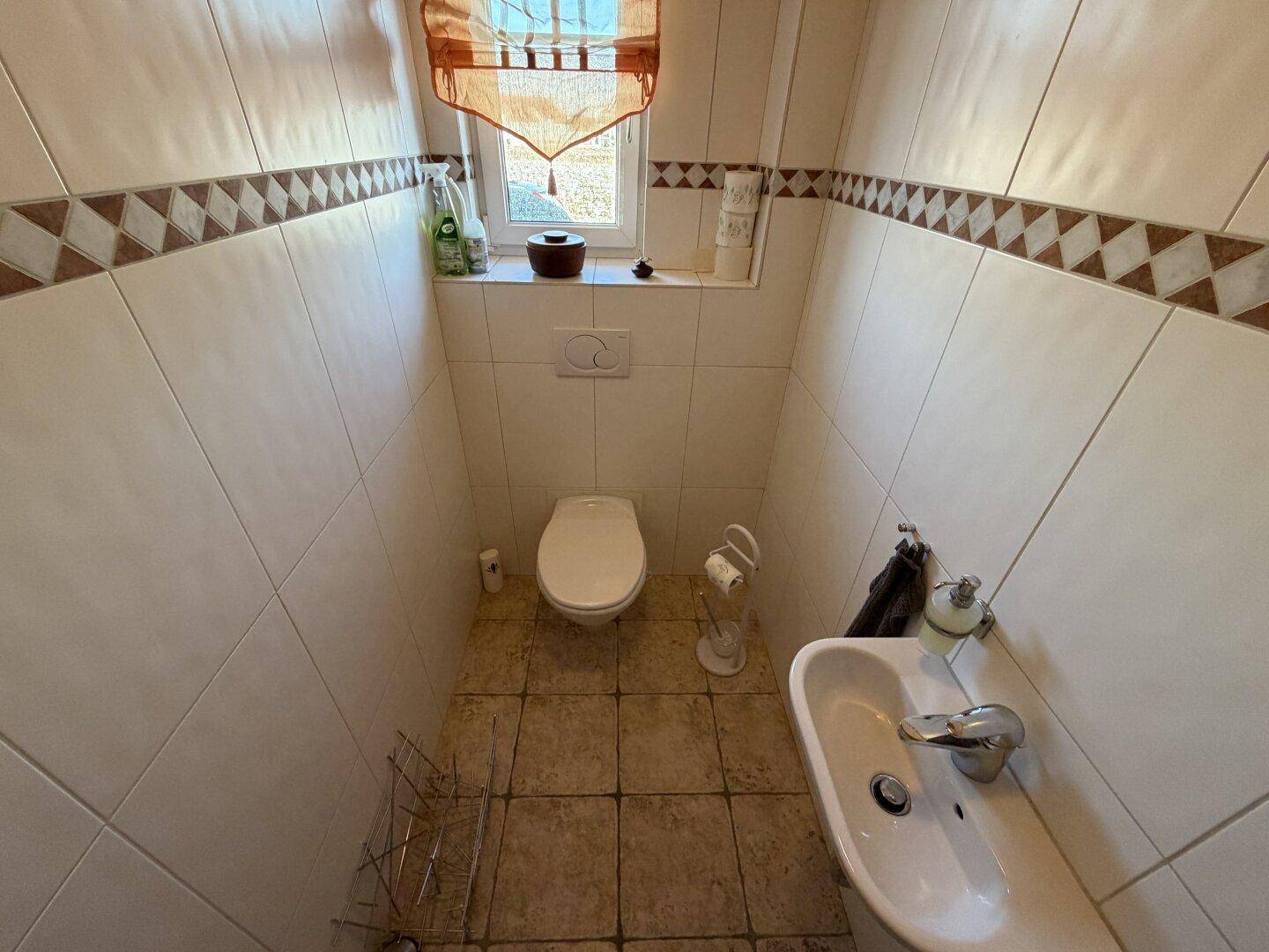 Kleines Gäste-WC mit Waschbecken, Toilette und einem Fenster für natürliche Belüftung.