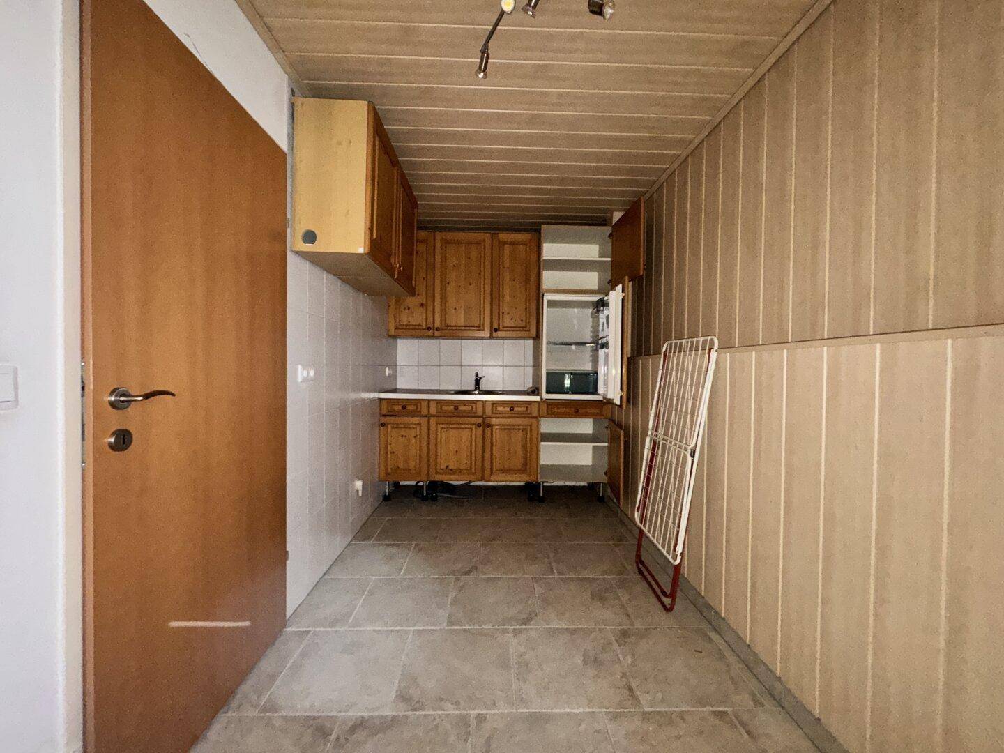 Kleine Küchenzeile im Untergeschoss mit Holzschränken und Fliesenboden.