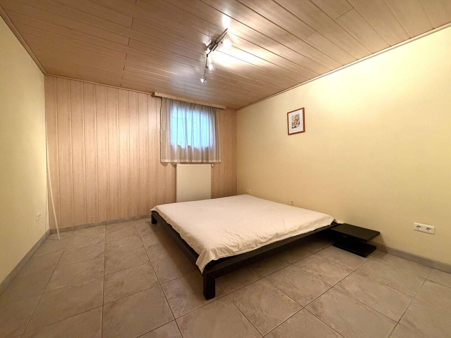 Schlafzimmer im Untergeschoss mit Bett, Fliesenboden und Holzverkleidung an Decke und Wand.
