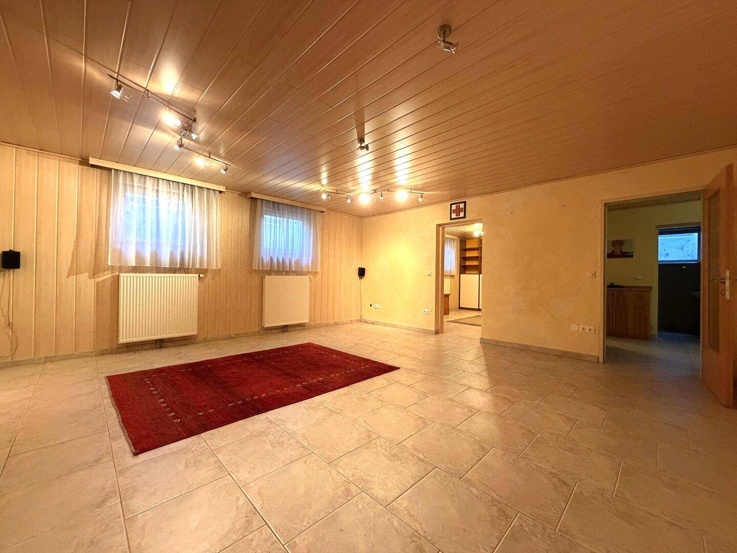 Geräumiges Wohnzimmer im Untergeschoss mit Teppich, Fliesenboden und Holzdecke.