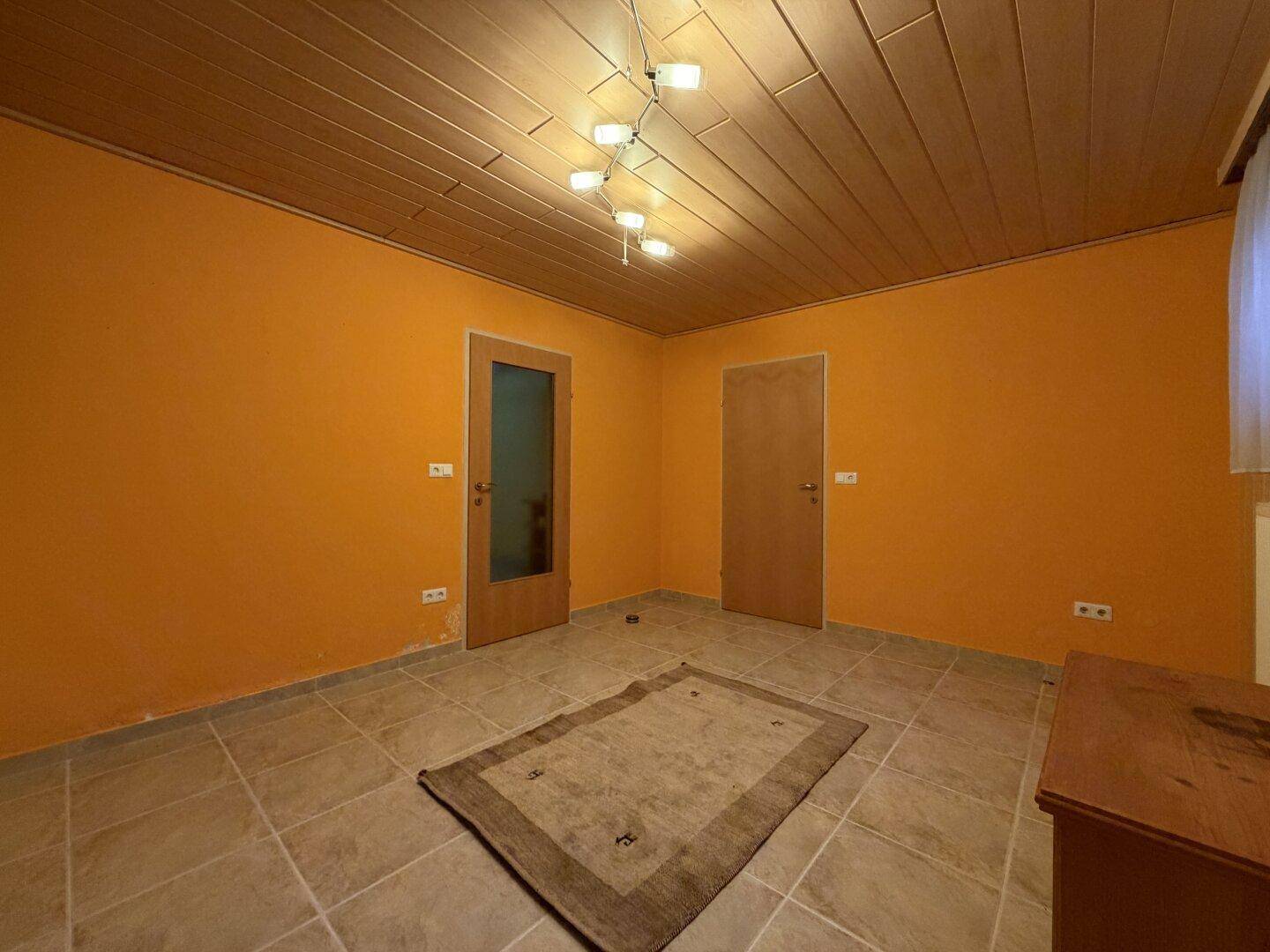 Raum im Untergeschoss mit orangefarbenen Wänden, Fliesenboden und Holzdecke.