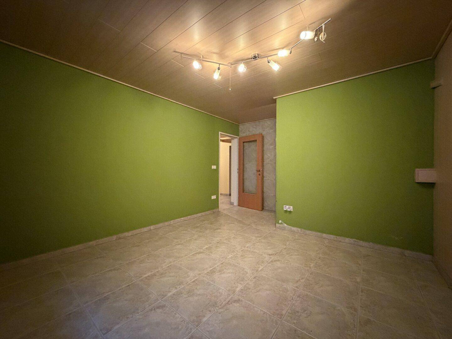 Raum im Untergeschoss mit grünen Wänden, Fliesenboden und Holzdecke.