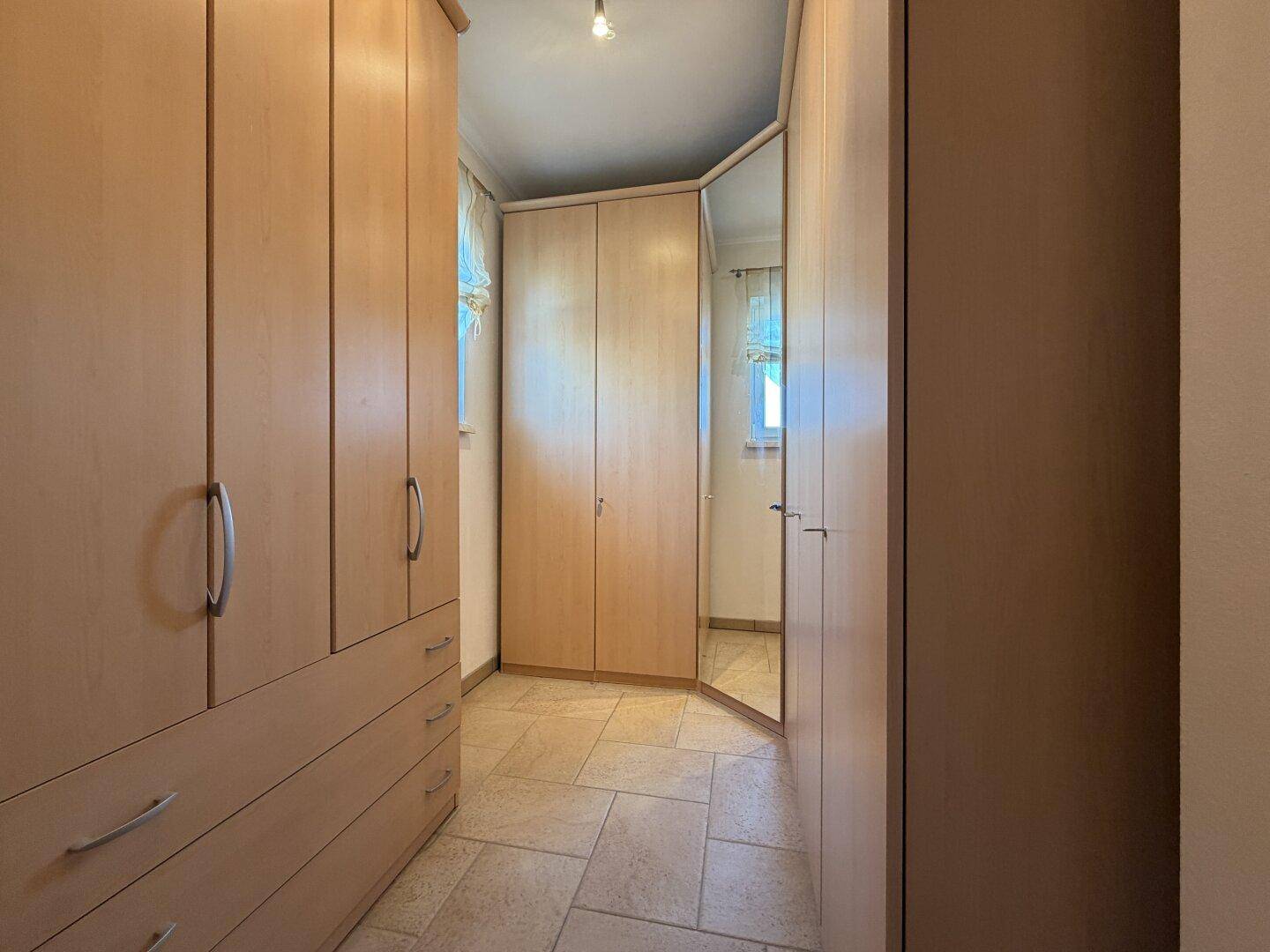 Praktischer begehbarer Kleiderschrank mit hellen Holzschränken und einem Spiegelschrank.