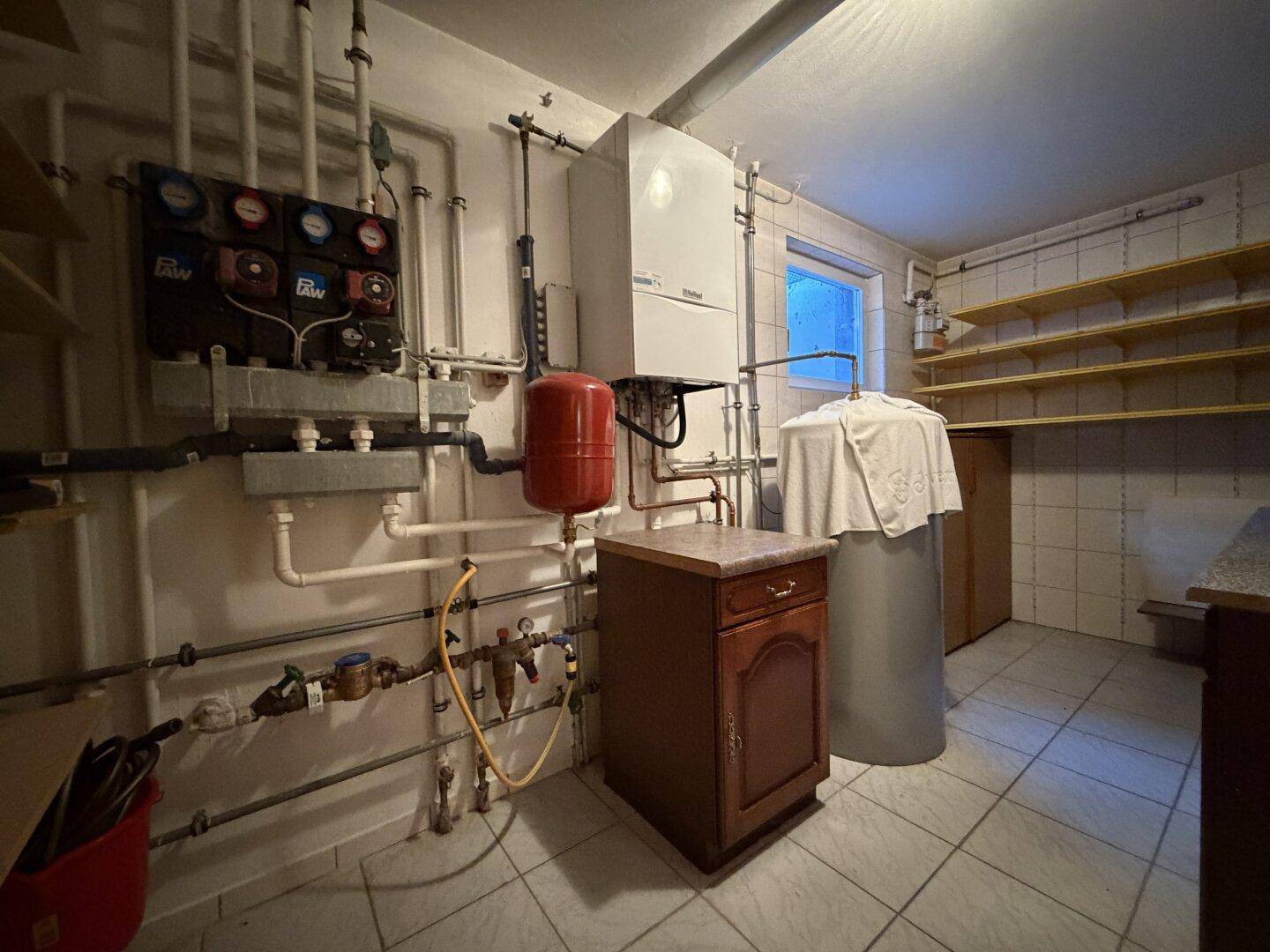 Heizungsraum im Untergeschoss mit Heizungsanlage, Rohren und Regalen.