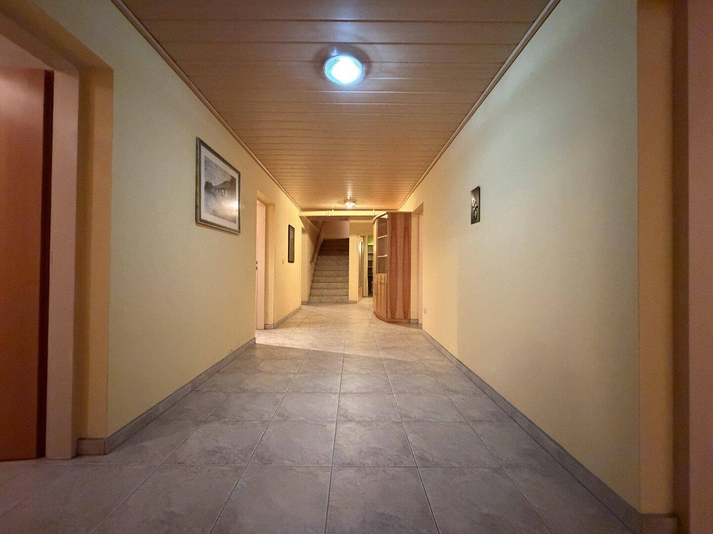 Langer Flur im Untergeschoss mit Fliesenboden, Holzdecke und Treppenaufgang.