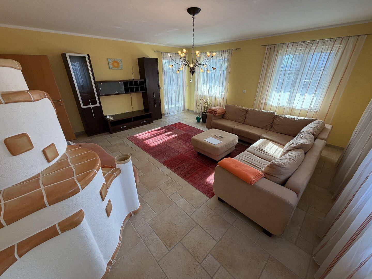 Gemütliches Wohnzimmer mit großem Ecksofa, traditionellem Kachelofen und gelben Wänden.