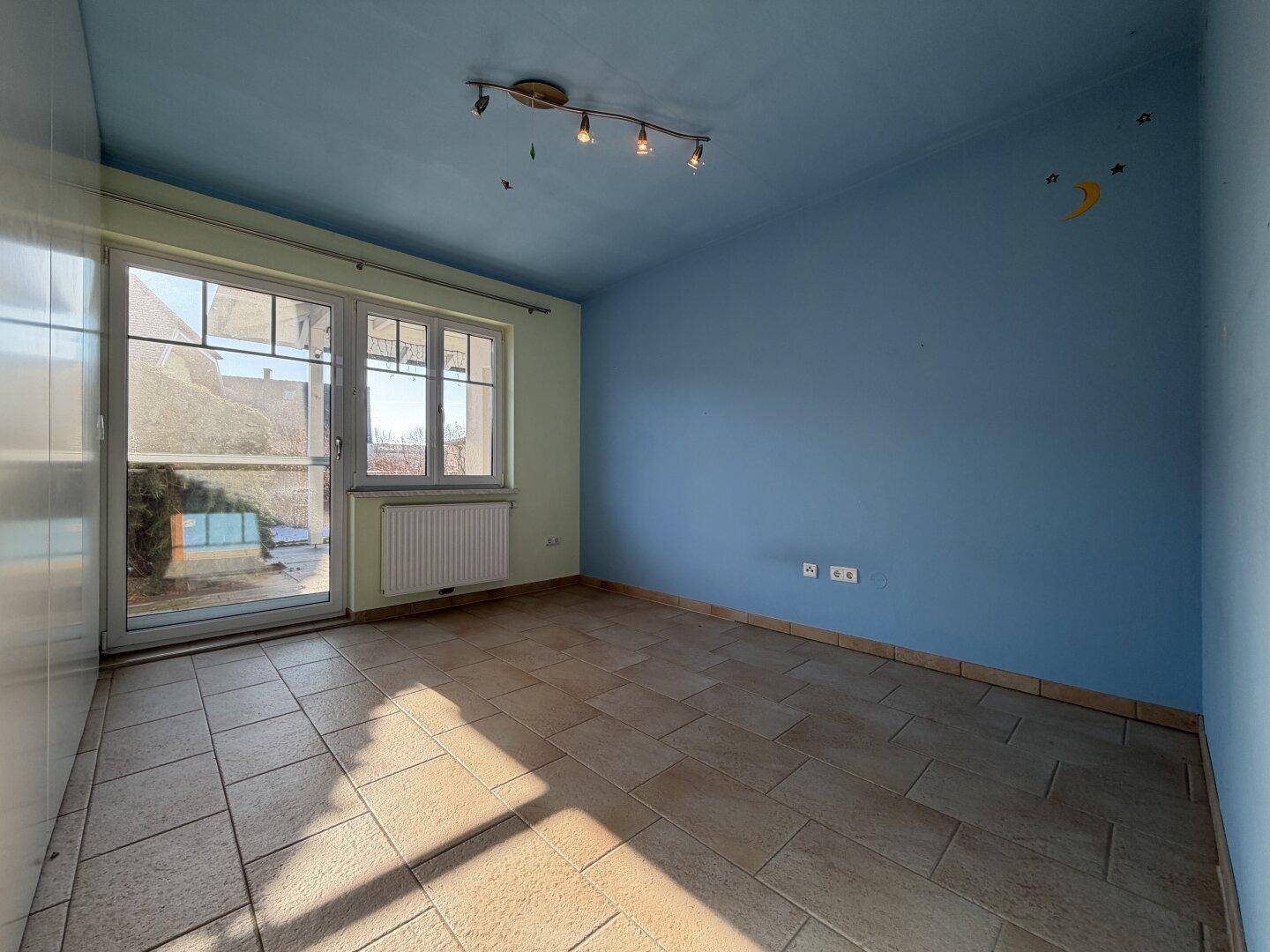 Raum mit blauen Wänden, Fliesenboden und einer Glastür, die ins Freie führt.