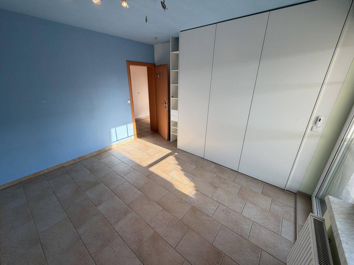 Heller Raum mit blauen Wänden, Fliesenboden und einem großen weißen Einbauschrank.