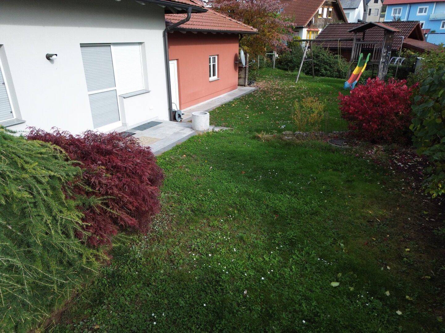 Gepflegter Gartenbereich mit Rasenfläche, Kinderrutsche und bunten Sträuchern im Herbst.