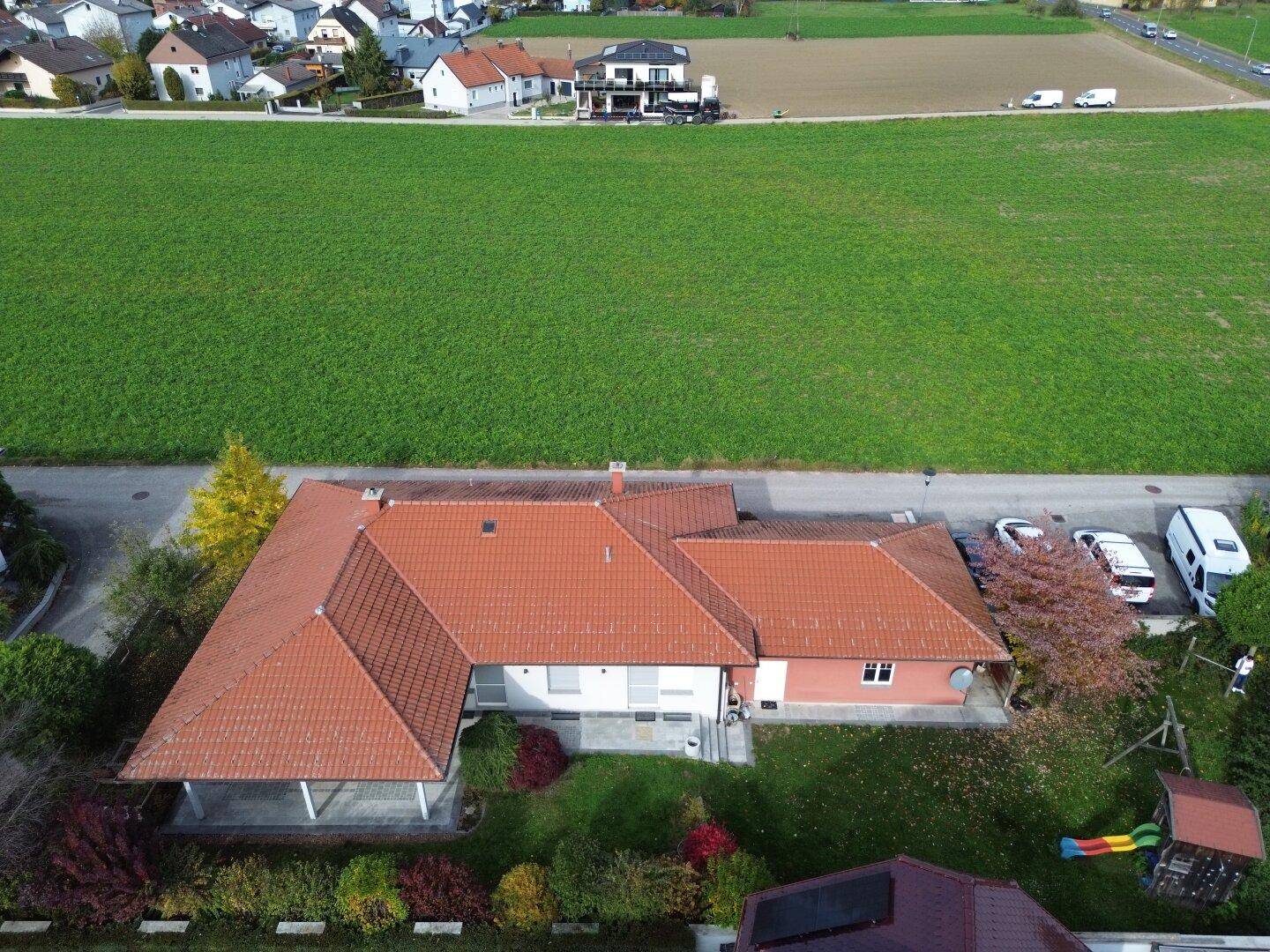 Sehr weite Luftaufnahme des Hauses mit weitläufigen Feldern und angrenzender Wohnsiedlung in der Ferne.