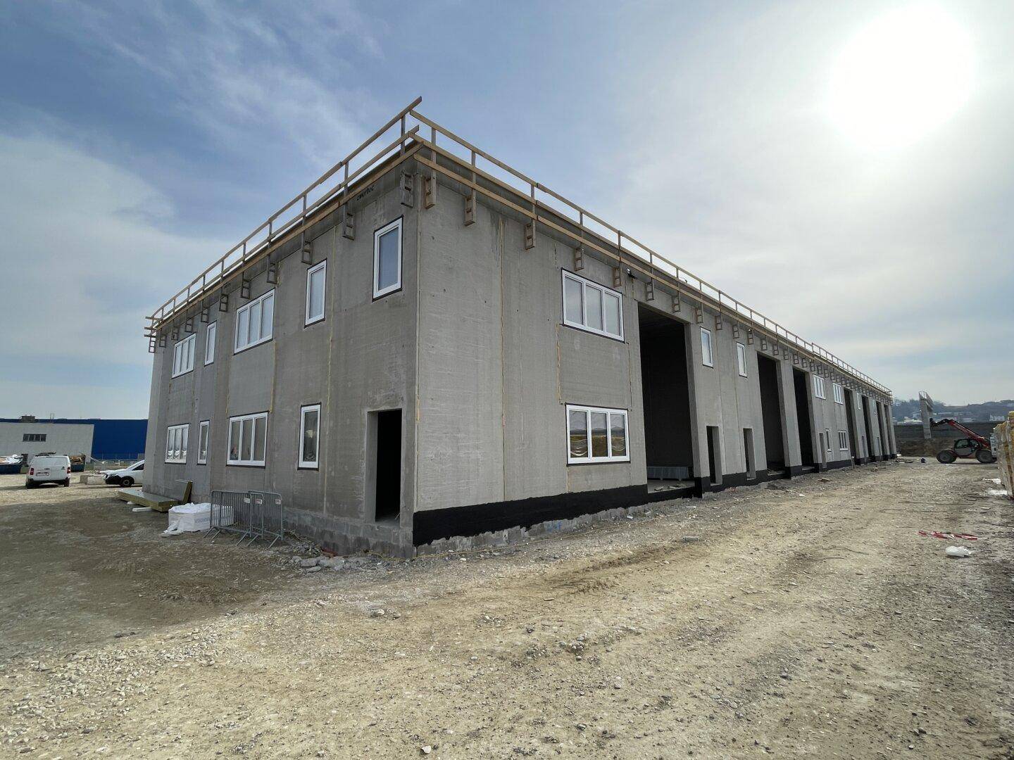 Gewerbegebäude im Bau mit Betonfassade, installierten Fenstern und Dachkonstruktion.