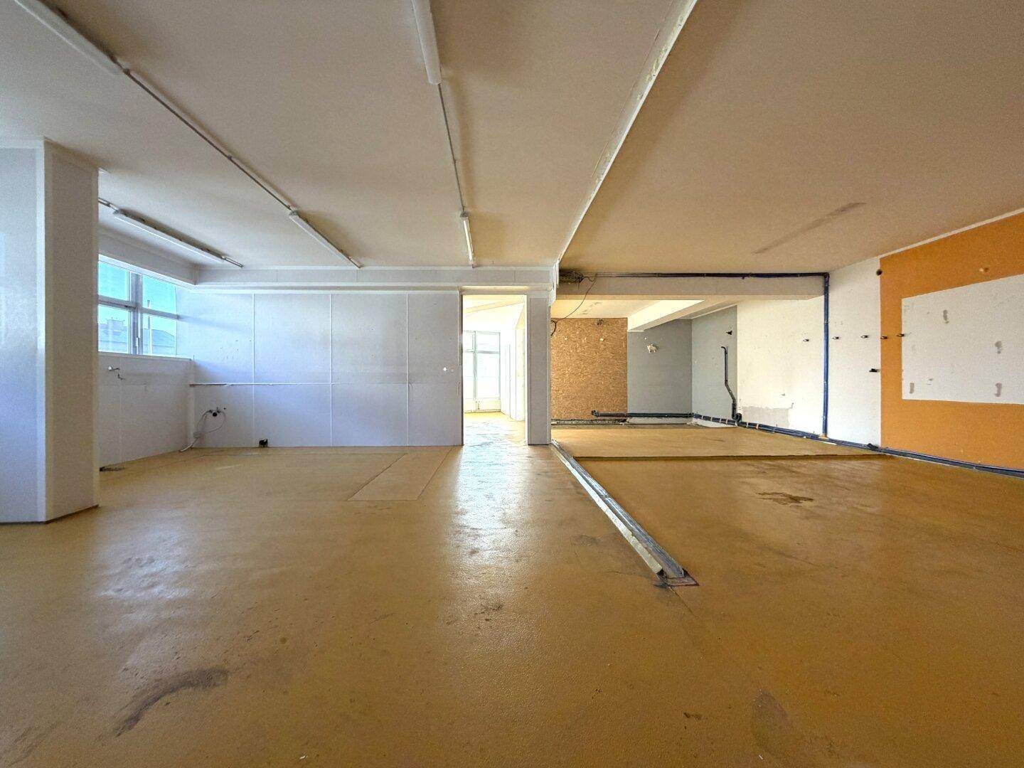 Geräumiger, unmöblierter Gewerberaum mit gelbem Boden und teilweise freigelegten Wänden, bereit für den Ausbau.