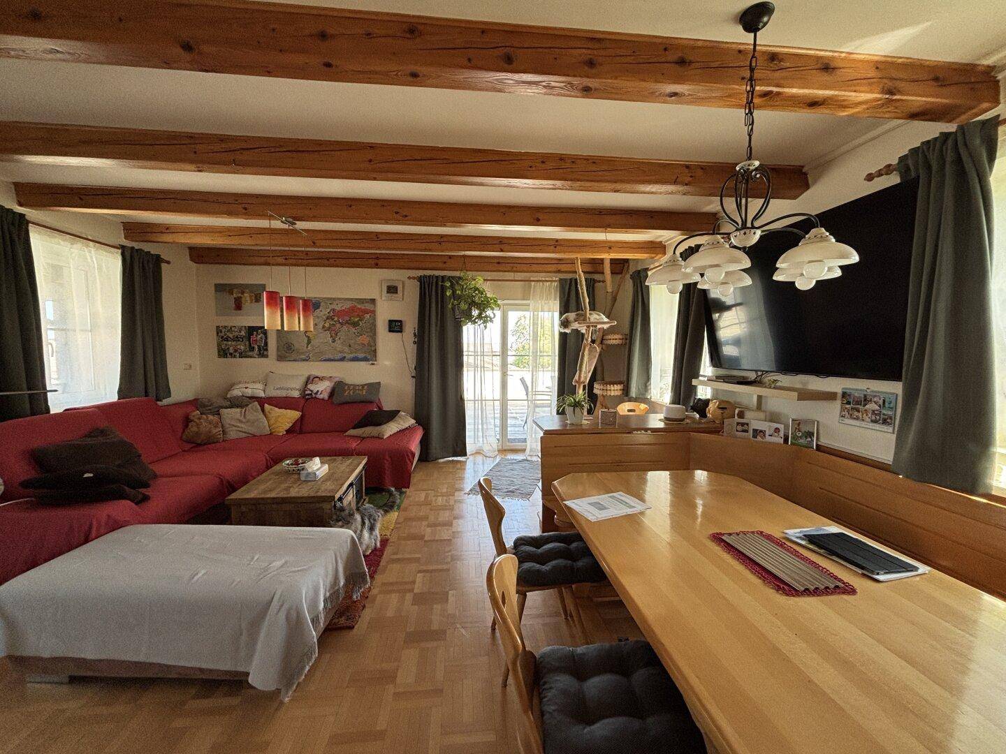 Geräumiger Wohn-Essbereich mit Holzbalken, Parkettboden und Zugang zur Terrasse.