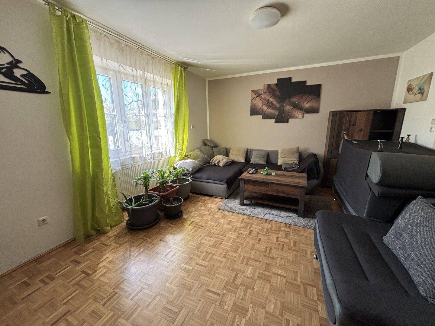 Helles Wohnzimmer mit Parkettboden, bequemer Couch und großen Fenstern.