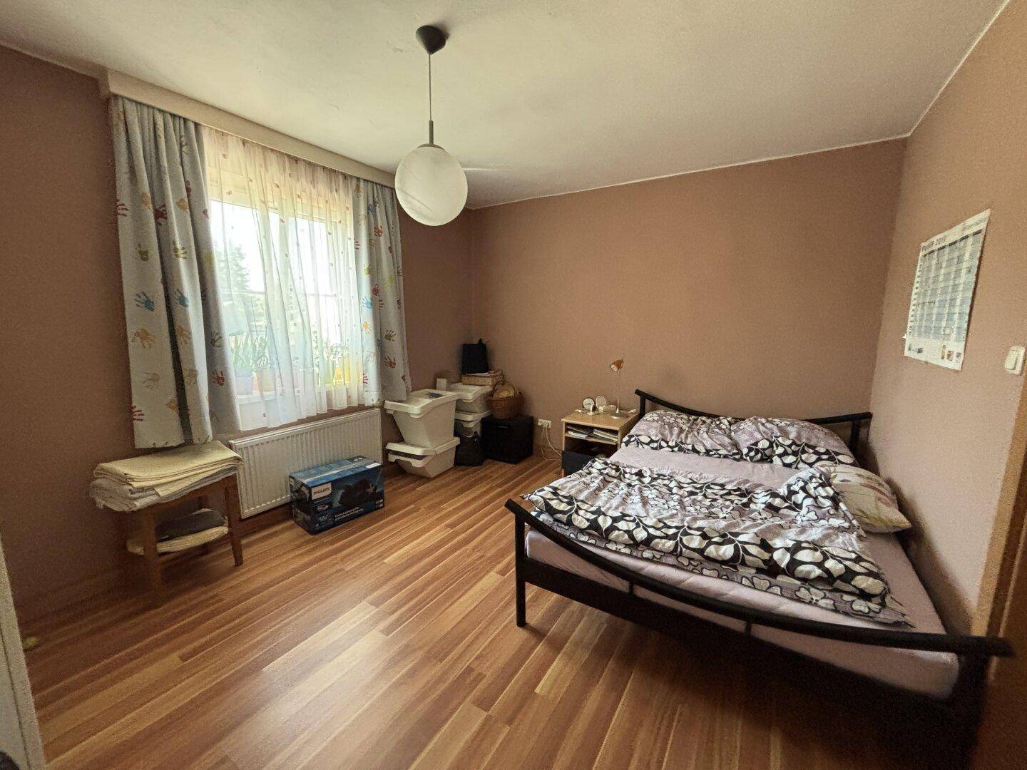 Schlafzimmer mit braunen Wänden, Holzfußboden und Fenster mit Vorhängen.