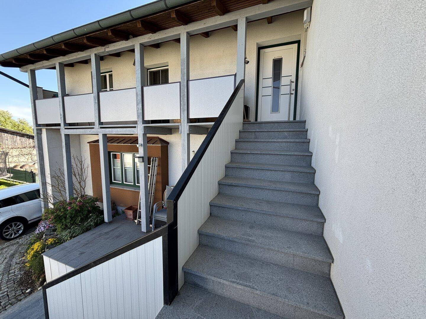 Außentreppe mit Steinstufen und Geländer, die zum oberen Eingang des Hauses führt.