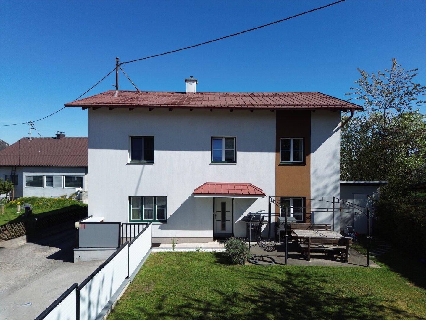Vorderansicht des Hauses mit weißer Fassade, rotem Vordach und einem kleinen Vorgarten mit Sitzbereich.