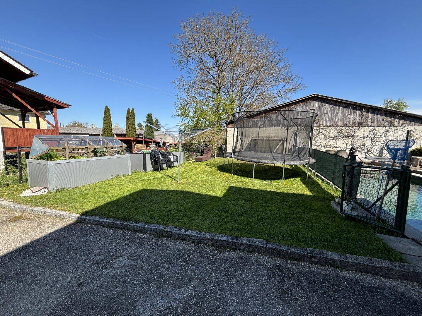 Gepflegter Garten mit Rasenfläche, Trampolin und Hochbeeten.
