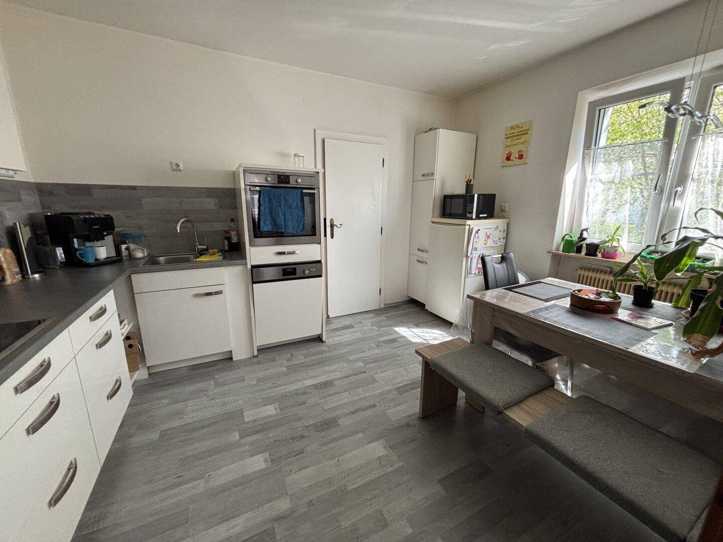 Helle Wohnküche mit Esstisch, weißen Schränken und Fenster mit Blick ins Grüne.