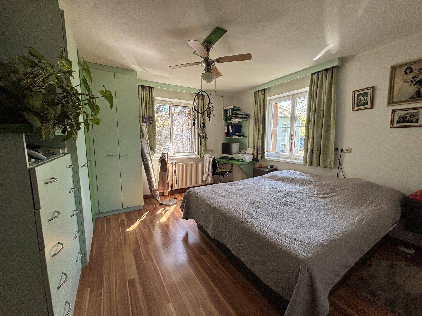 Helles Schlafzimmer mit Holzfußboden, grünen Wänden und Deckenventilator.
